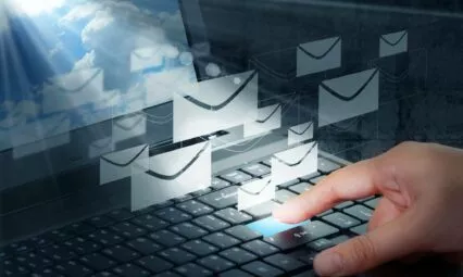Main appuyant sur une touche de clavier avec des icônes d'e-mails flottants, illustrant une campagne d'emailing.
