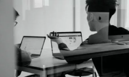 Deux personnes travaillant sur des ordinateurs portables dans un bureau, illustrant la communication corporate.