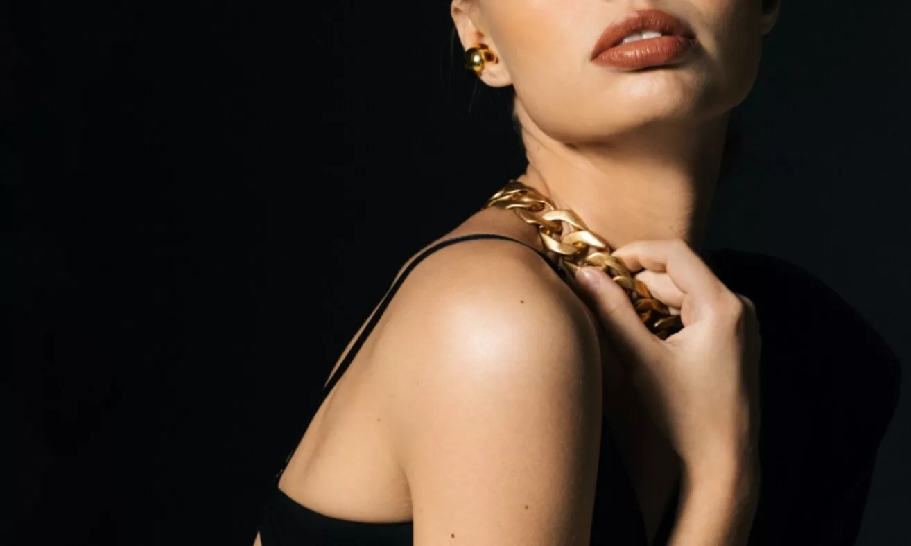Femme élégante portant un collier doré, photographiée sur fond noir par Actif Digital.
