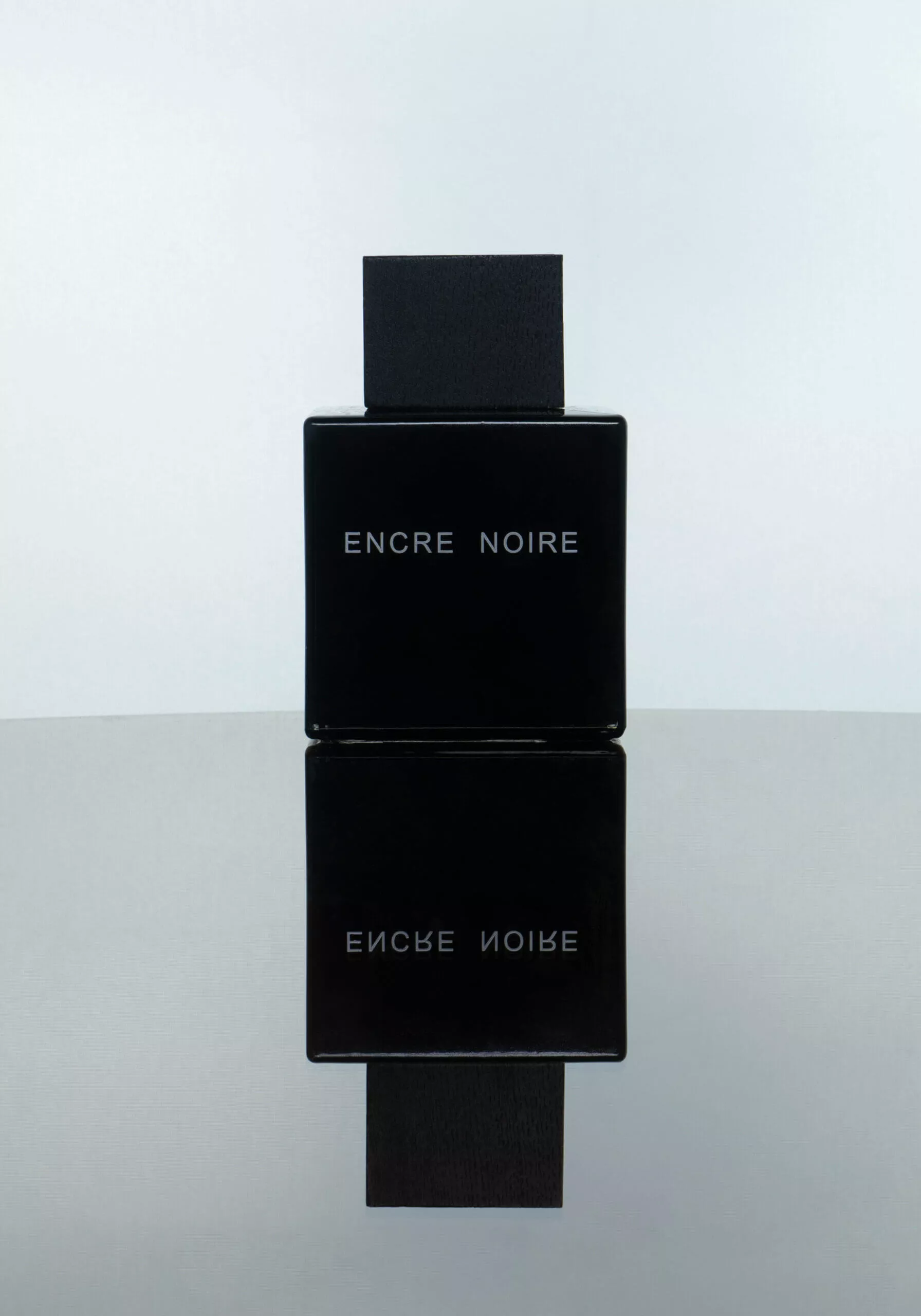 Flacon de parfum Encre Noire, photographié sur un fond clair avec son reflet visible.