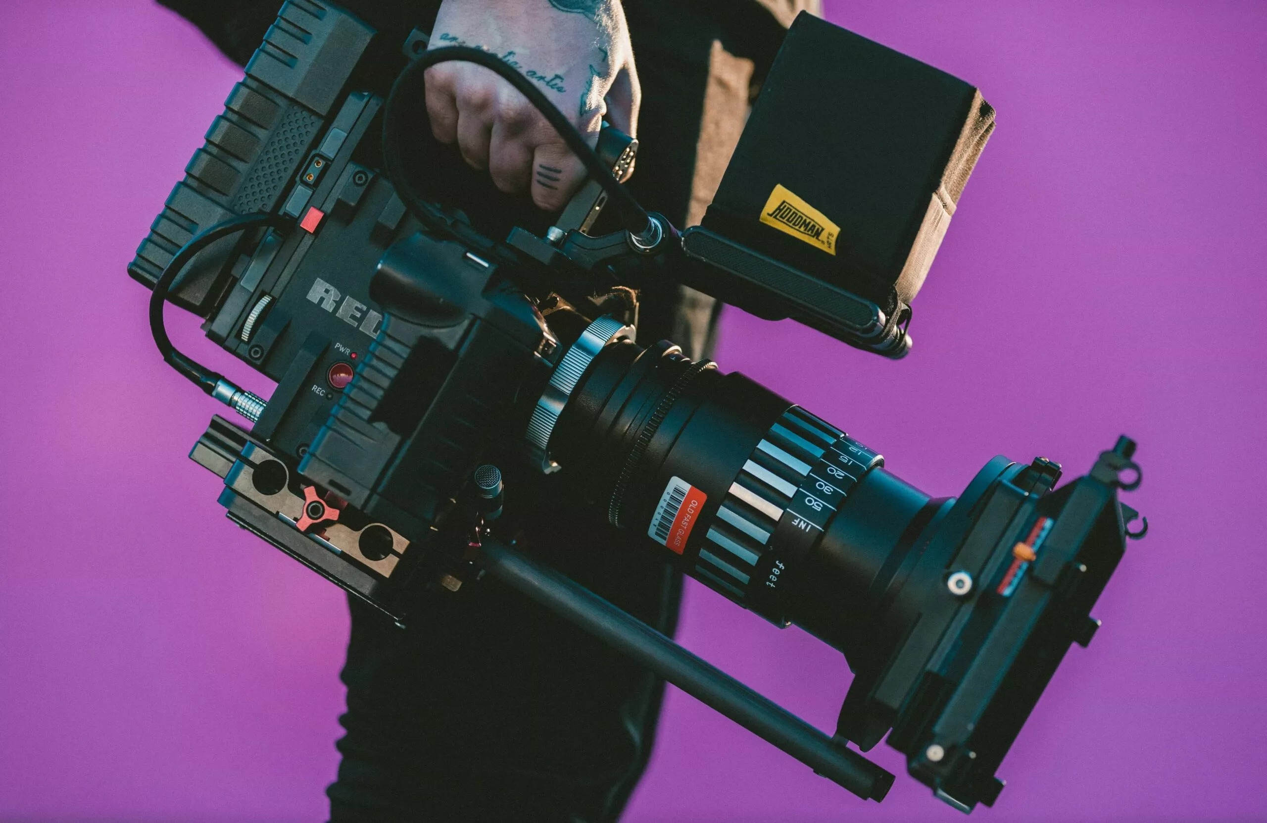 Main d'un caméraman tenant une caméra RED, fond violet.